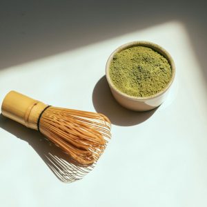Minimalist composition featuring matcha powder and bamboo whisk in sunlight.
