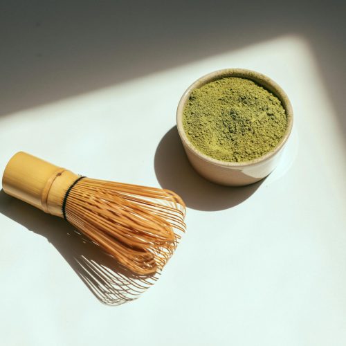 Minimalist composition featuring matcha powder and bamboo whisk in sunlight.